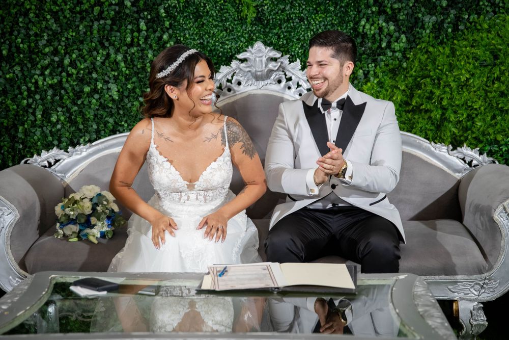 Couple shares candid moment on elegant grey sofa against green hedge wall.