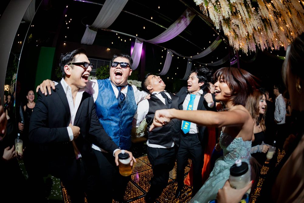 Party guests dancing and laughing under a chandelier at an indoor celebration.