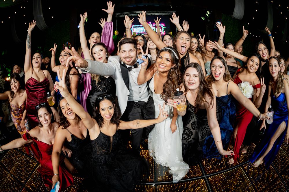 Large group celebrating at a wedding reception with hands raised in excitement.