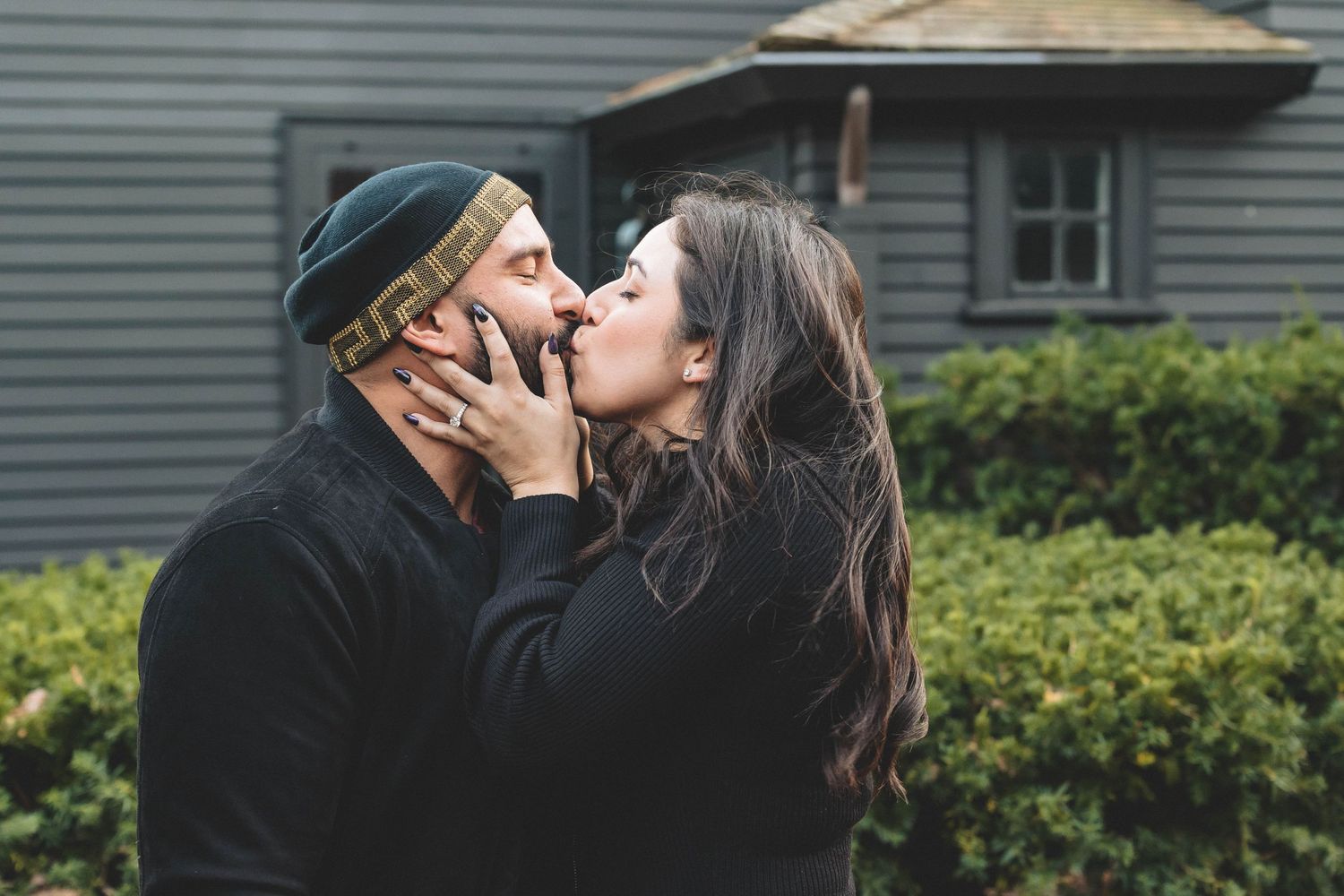 A romantic moment shared between two people wearing dark clothes outdoors.