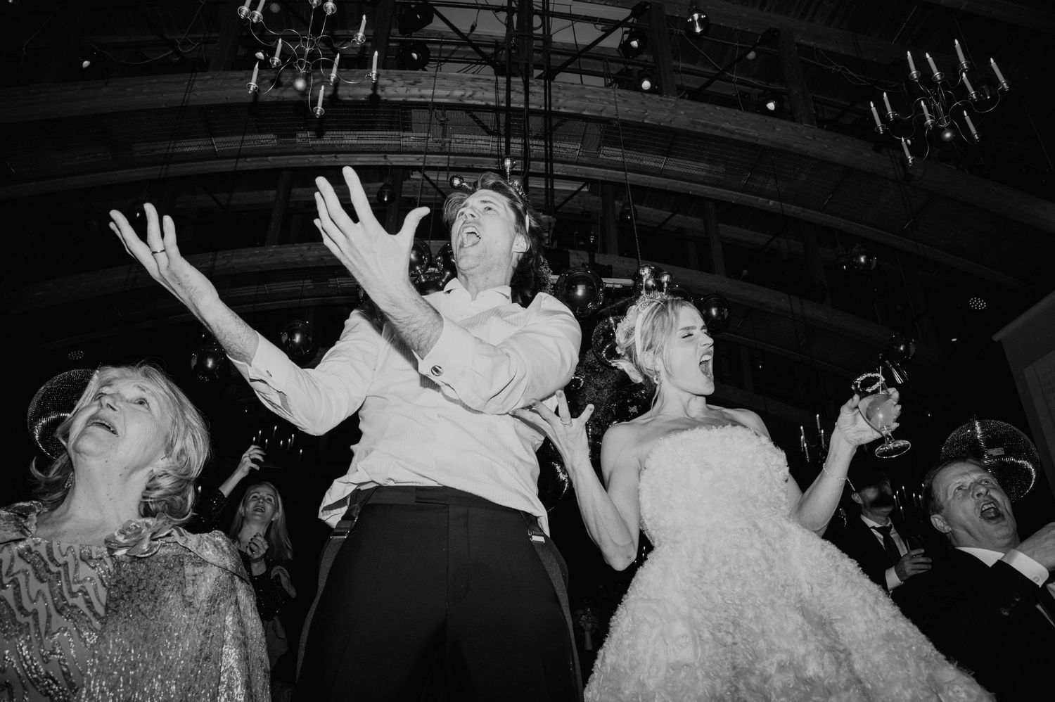 Black and white photo of wedding guests dancing with arms raised on crowded dance floor.