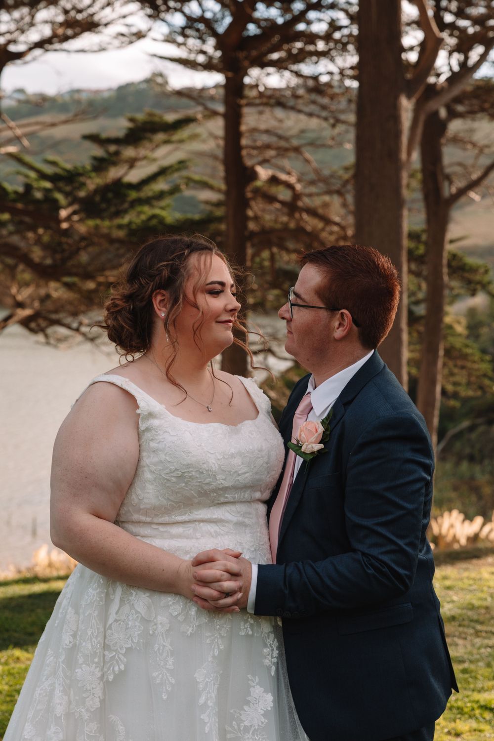 Happy couple sharing intimate moment under pine trees at outdoor wedding.