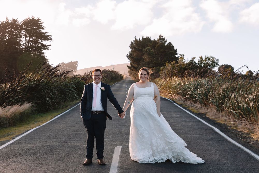 Wedding couple poses on empty road surrounded by coastal vegetation.