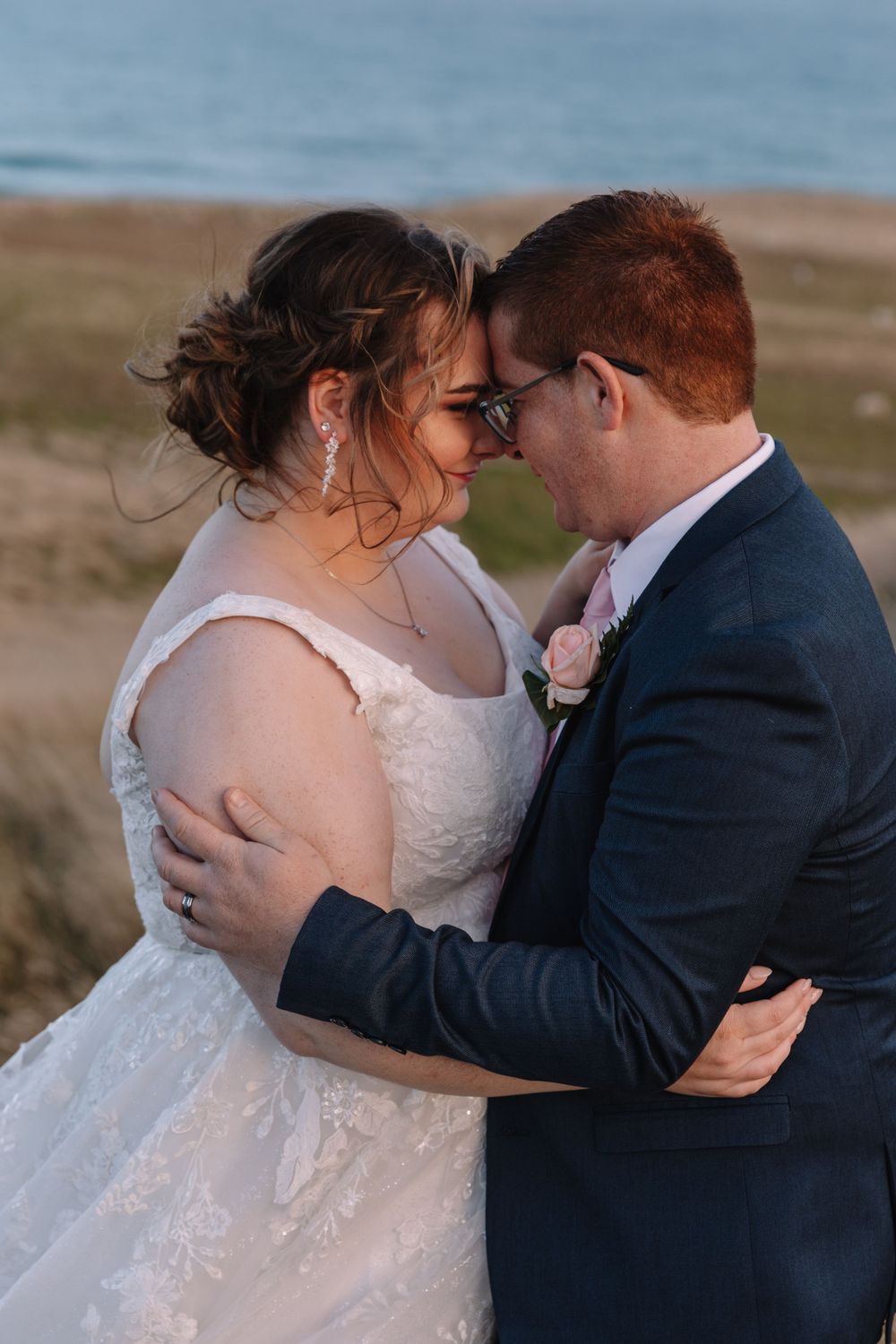 An intimate wedding portrait showing a tender moment between newlyweds on a coastal clifftop.