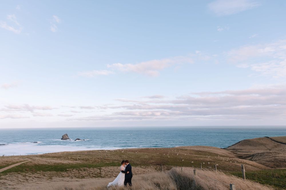 A distant view of newlyweds standing on a coastal path with dramatic ocean views.
