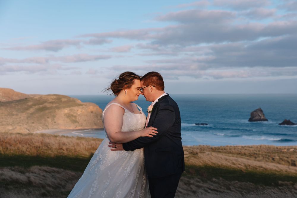 Romantic sunset wedding portrait with dramatic coastal cliffs and ocean backdrop.