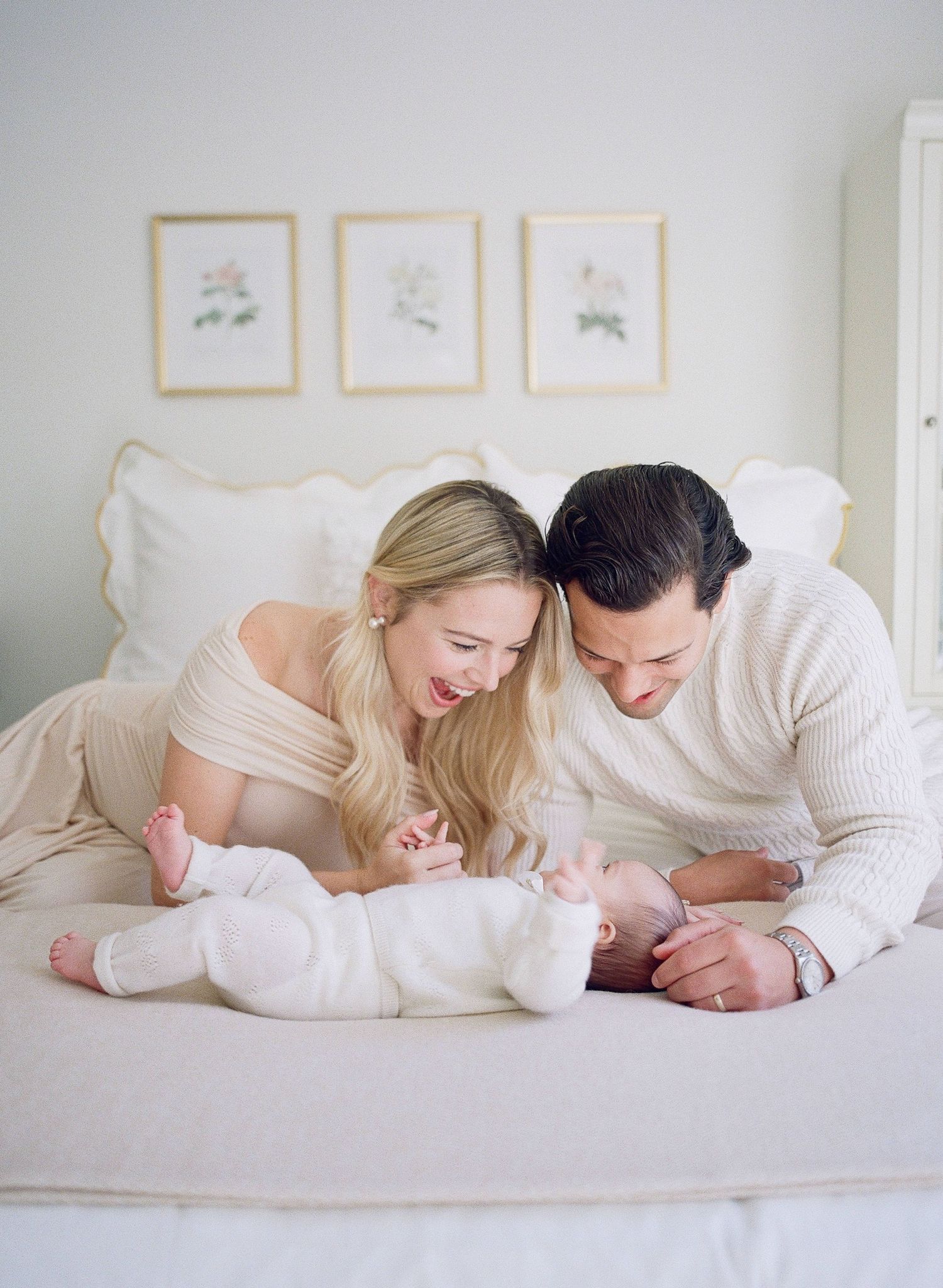 Family moment on white bedding with delicate wall art in the background.