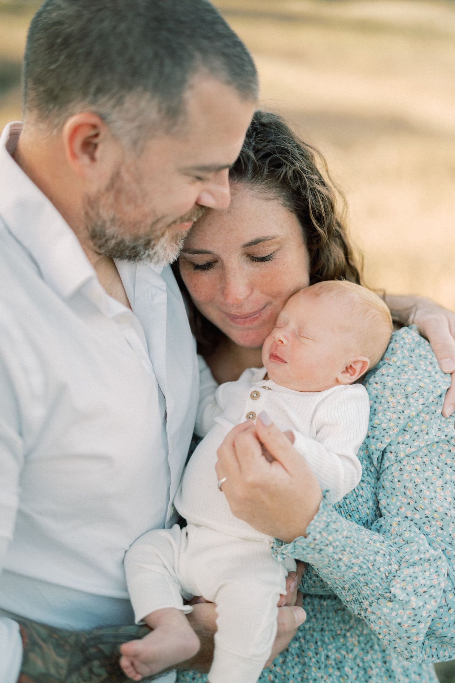 Intimate family portrait outdoors with parents embracing their sleeping newborn.