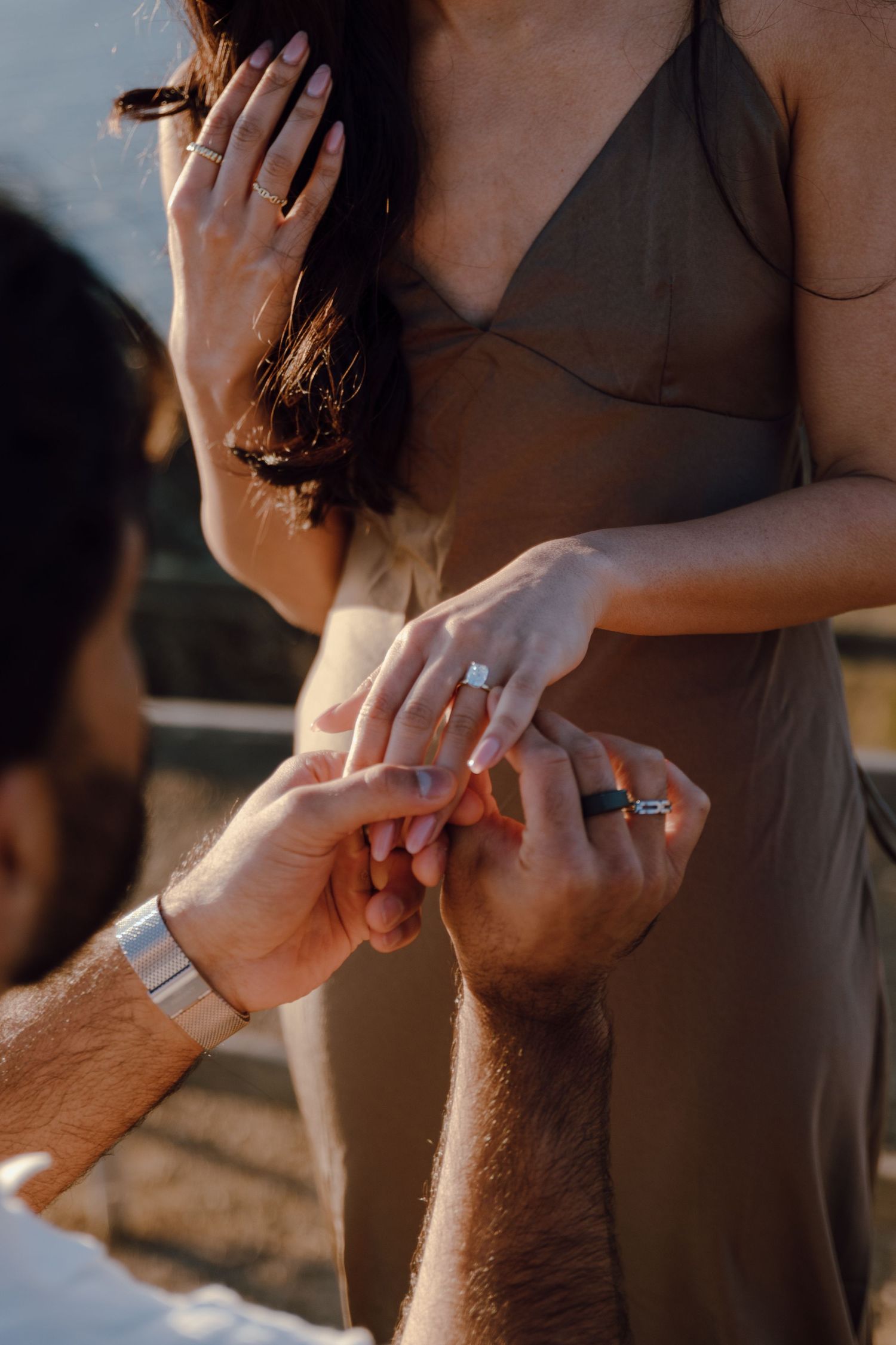 Close-up of engagement ring moment with hands in golden sunlight.