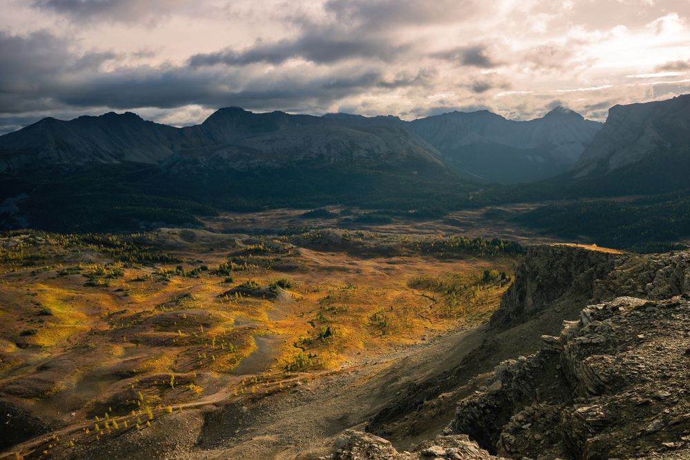 Rolling mountain valley with golden autumn colors under dramatic cloudy skies.