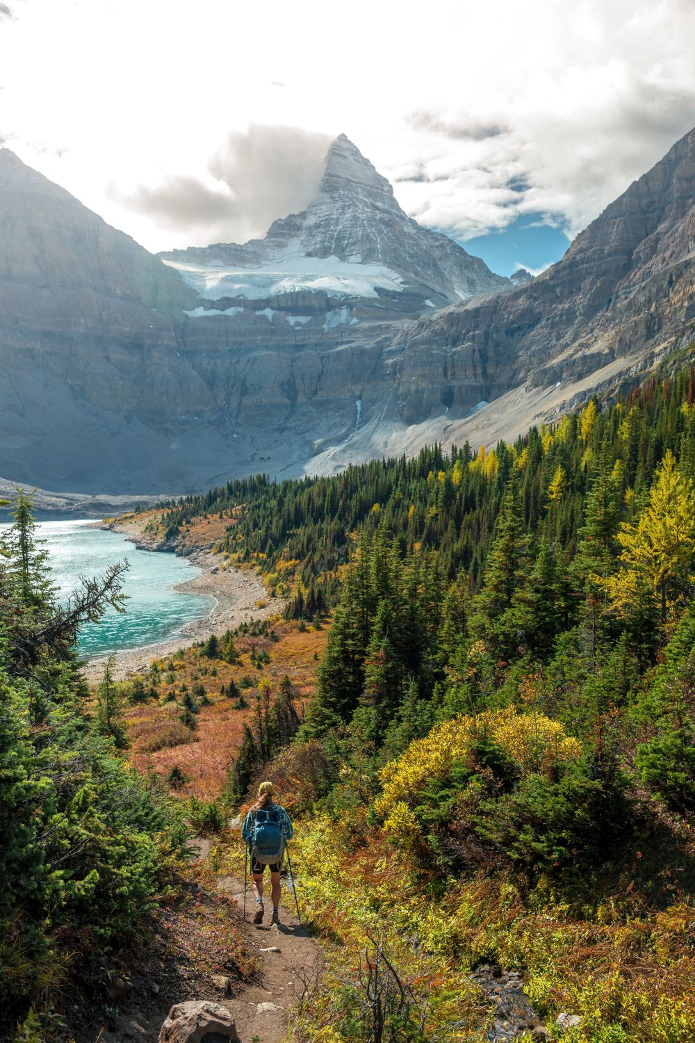 Hiking trail descends through fall foliage with turquoise river and mountain views.