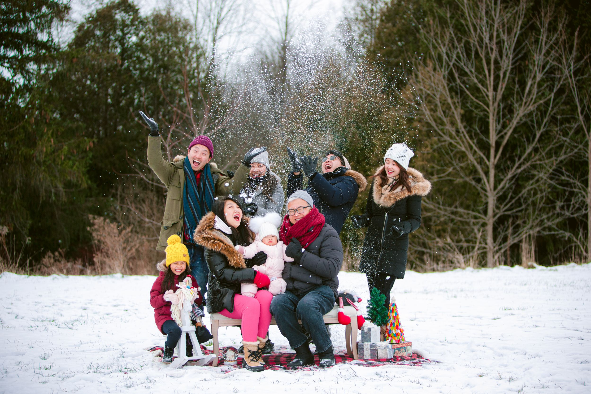 A group enjoys winter fun together posing in the snow on a cold day with trees in the background.