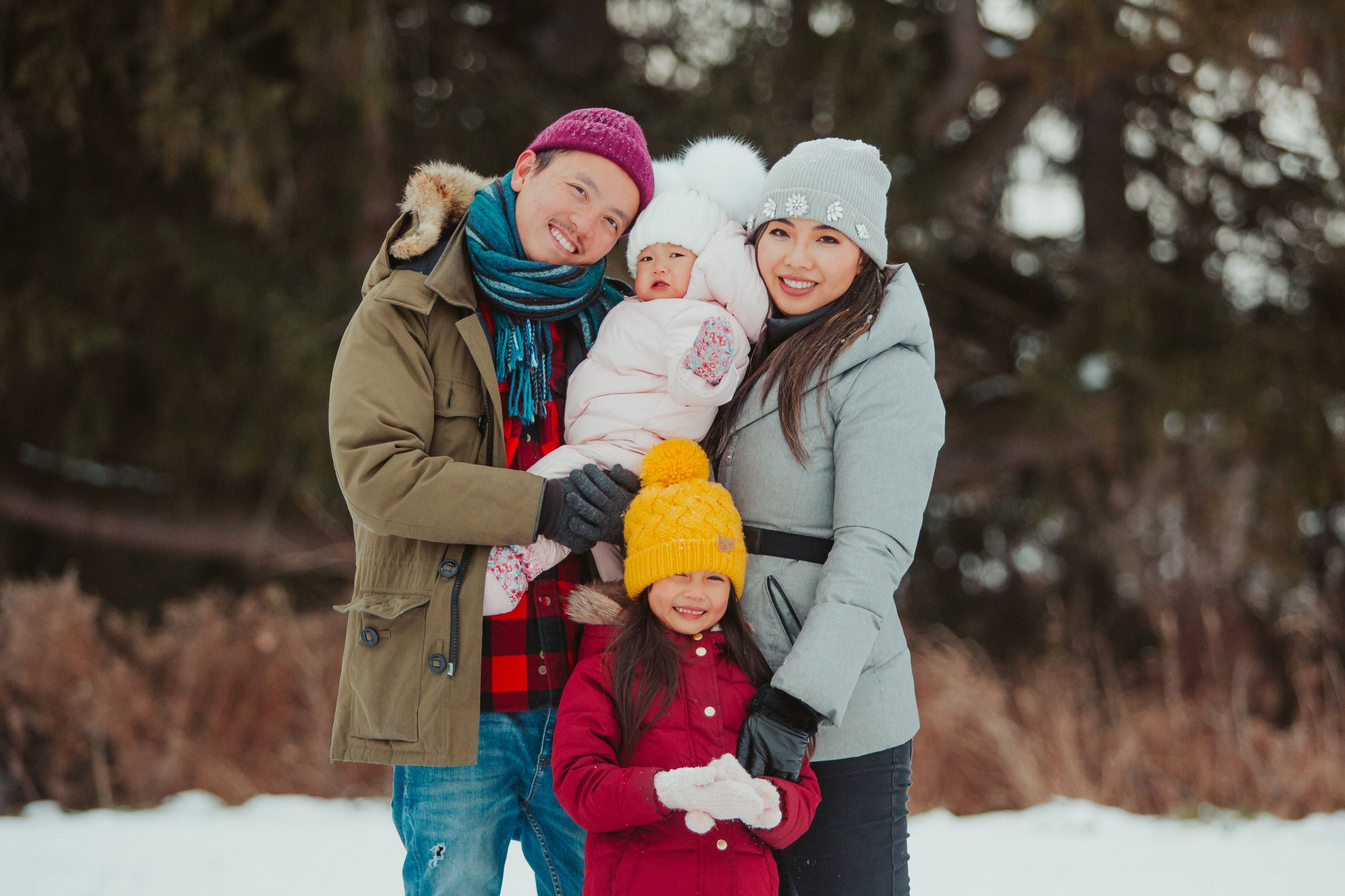 A family wearing winter coats poses together outdoors in the snow during a cold winter day.
