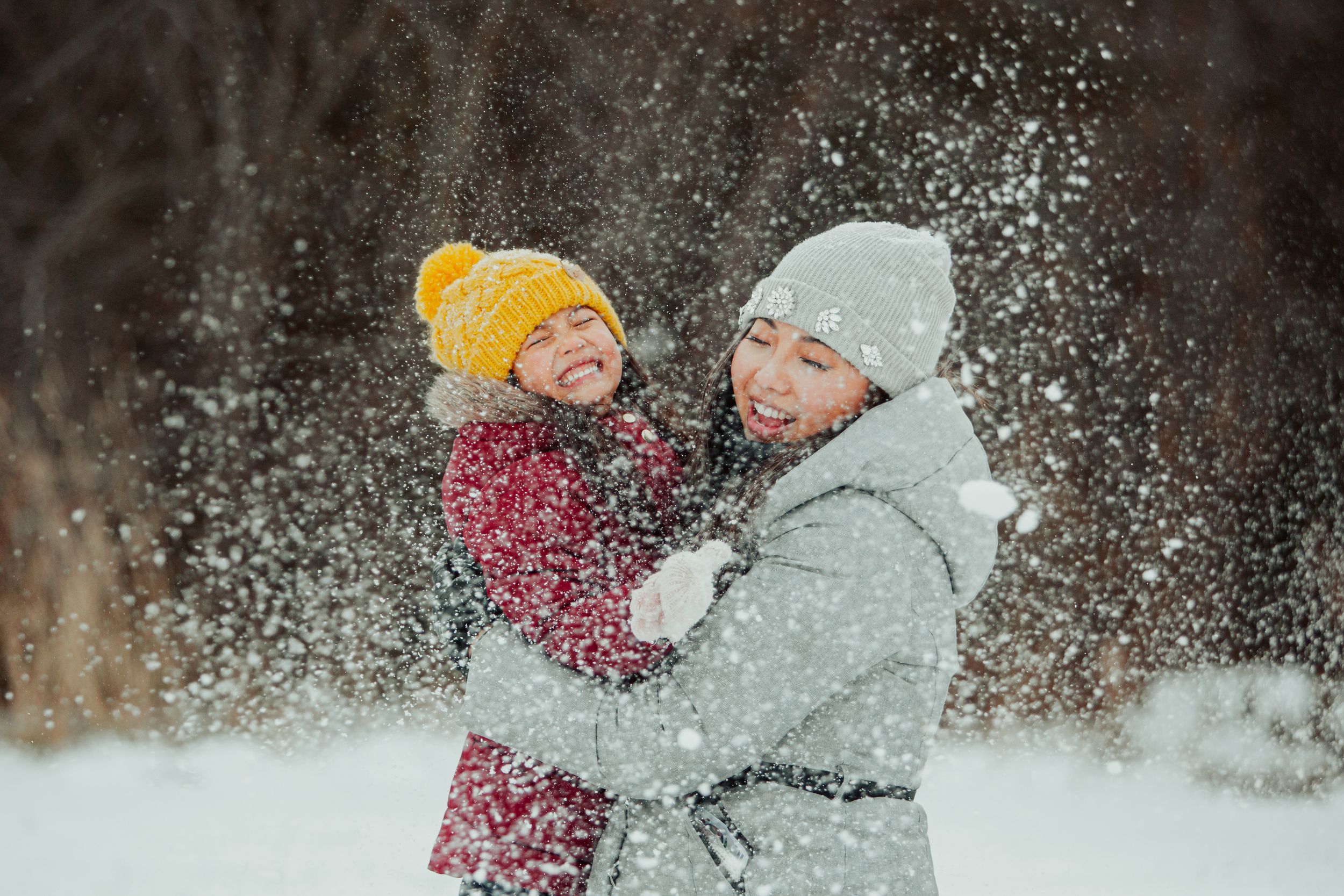 A parent and child play together in falling snow, wearing winter coats and knit hats.