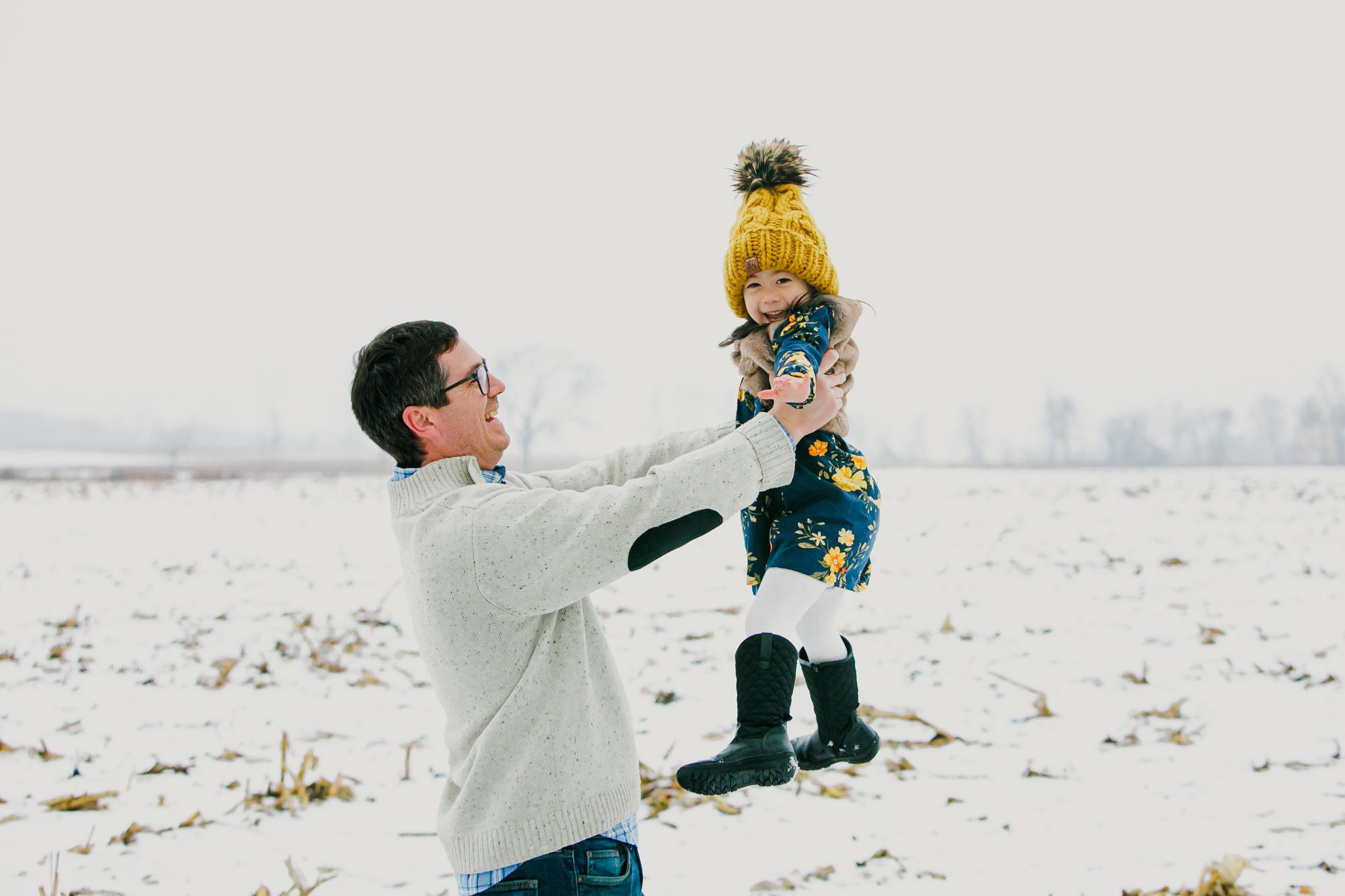 Two figures play together in a snowy winter field on a bright overcast day.