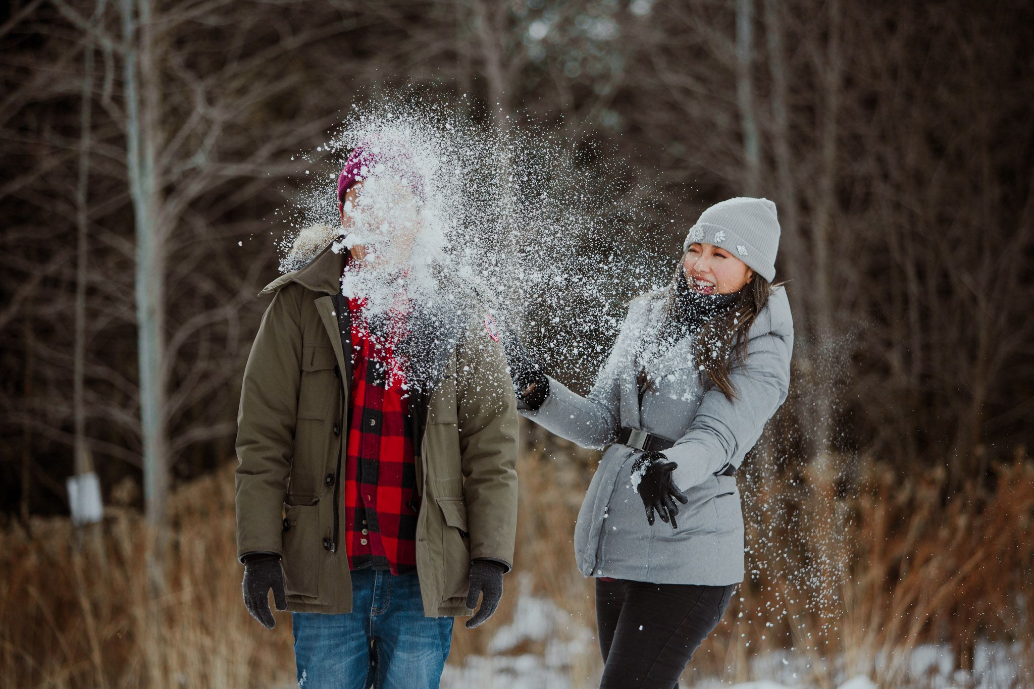 Two winter figures play in the snow as one throws powder at the other creating a misty effect in the cold winter light.