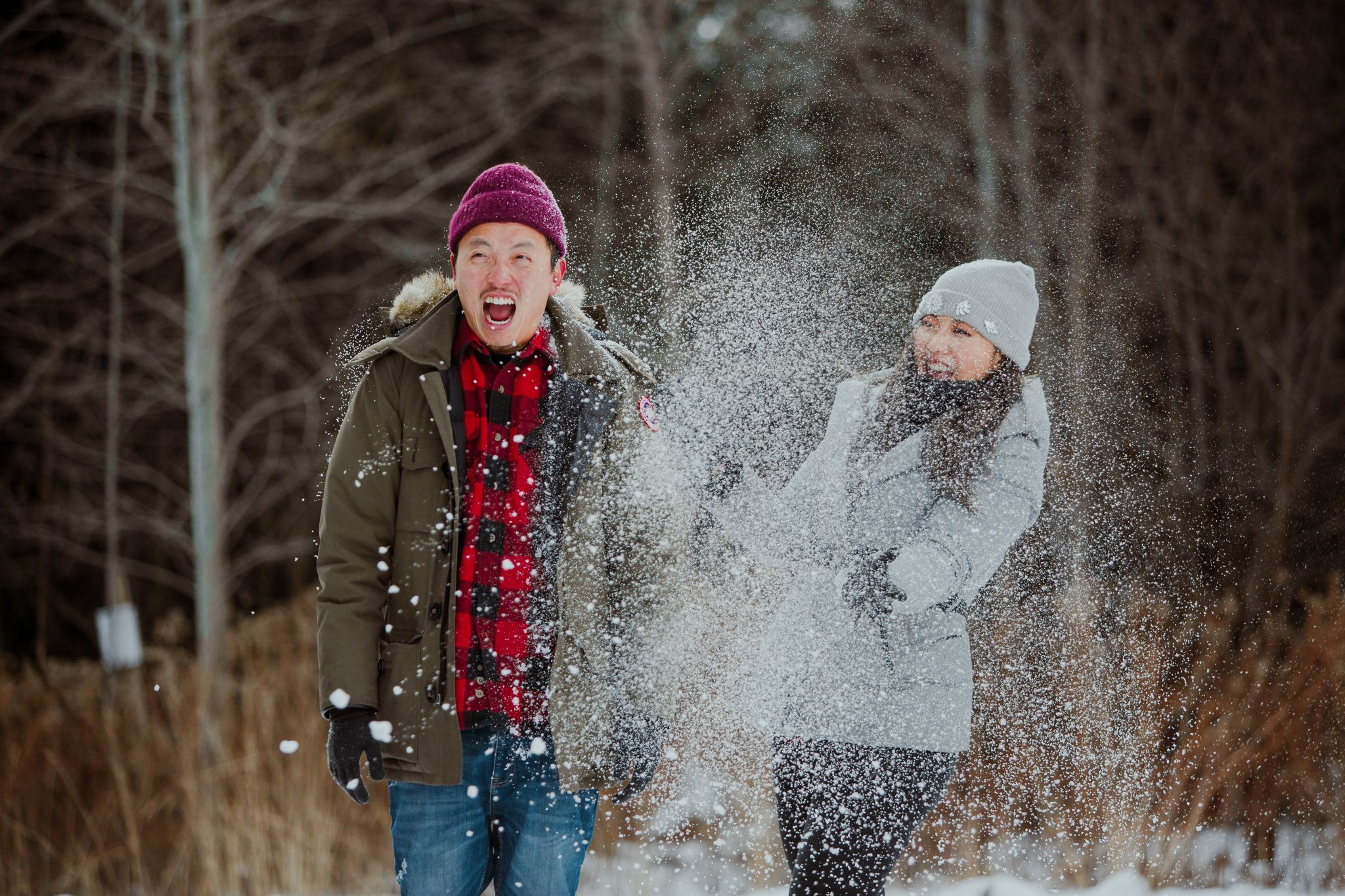 Two people playfully throwing snow at each other while enjoying a winter day in nature.