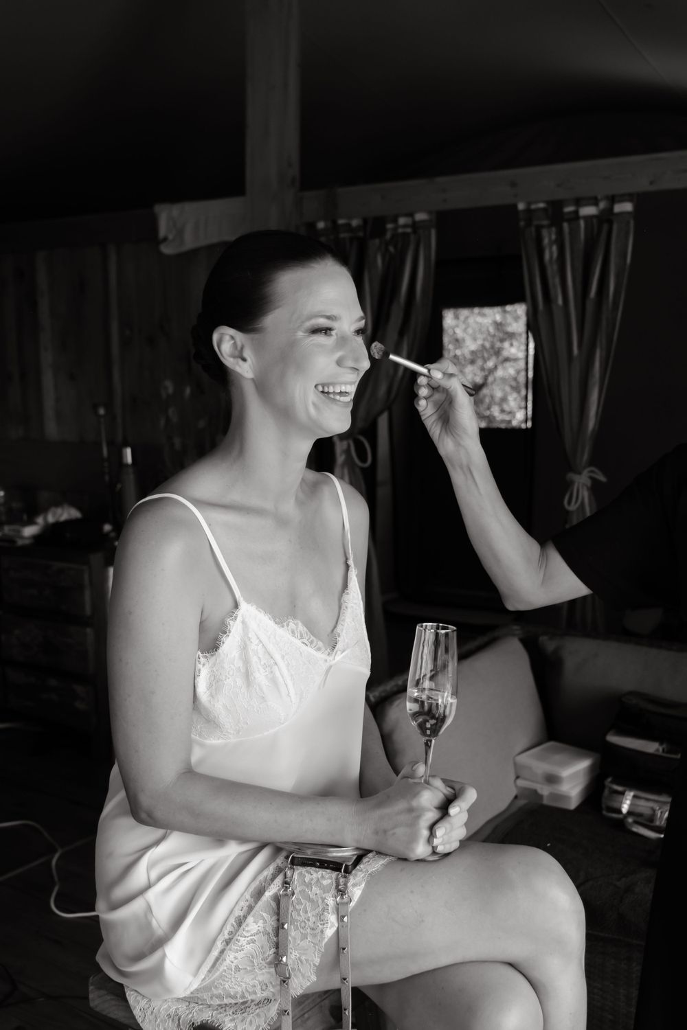 A joyful moment during wedding preparations as someone gets makeup done while holding a glass of champagne.