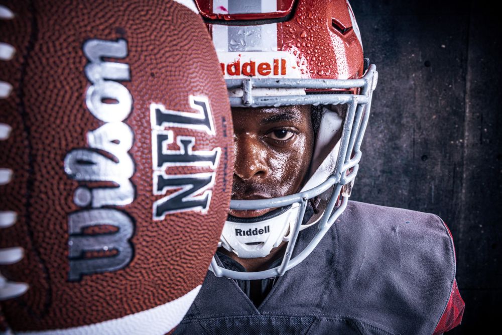 Close-up photo of an NFL football with blurred player wearing red helmet and facemask in background.