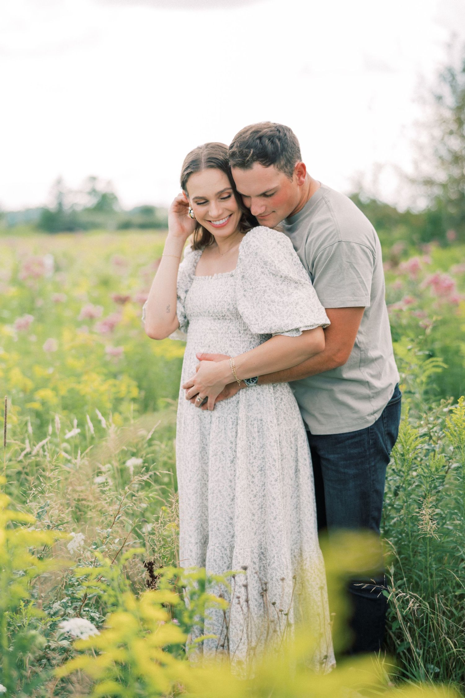 Intimate maternity portrait of couple embracing in blooming wildflower meadow.