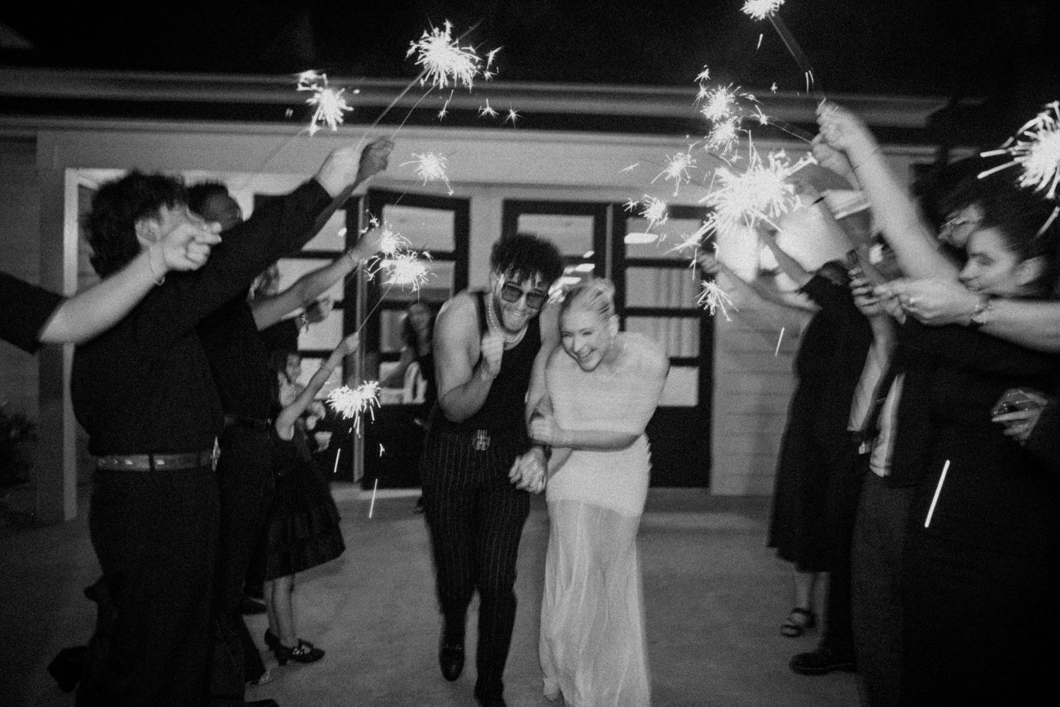 A black and white photo of wedding guests holding sparklers to create a magical send-off tunnel at nighttime.