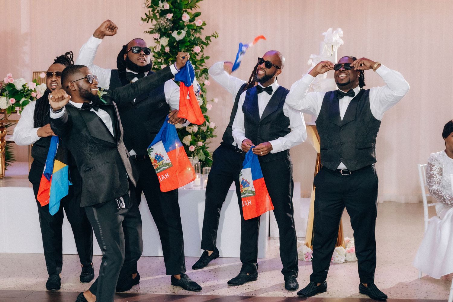 Groomsmen in formal attire performing a coordinated dance move at wedding reception.
