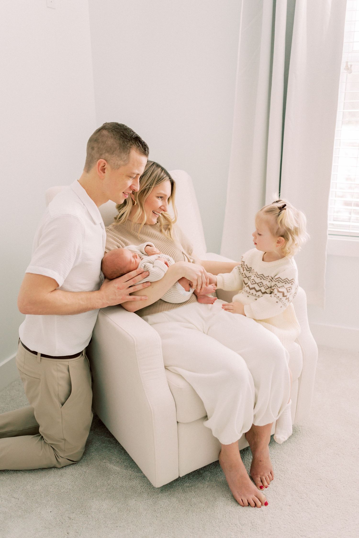 Family spending quality time together on white couch while holding newborn baby at home.