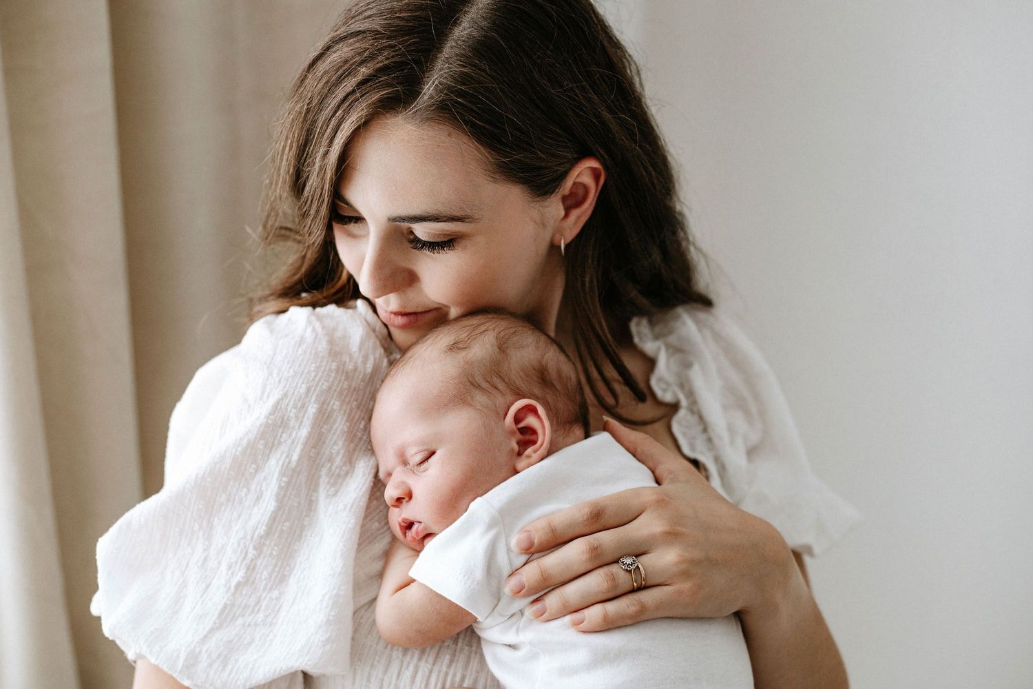 A peaceful sleeping baby in a knit sweater gently holds an adult's finger.