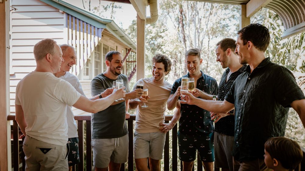 Friends gather on a porch toasting with drinks while celebrating together during a casual outdoor gathering.