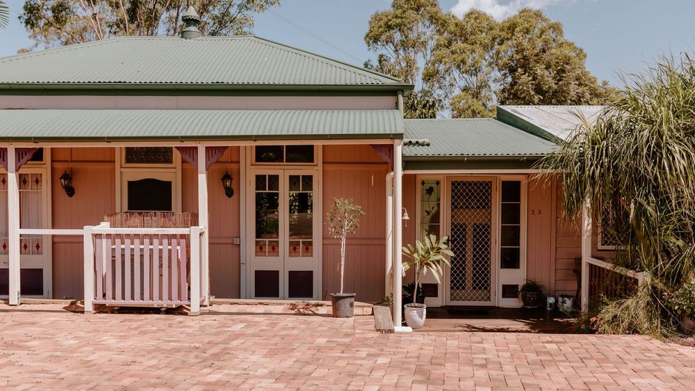 Rustic cottage exterior with pink walls, white trim and wraparound verandah surrounded by tropical landscaping.
