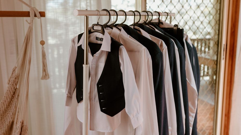 Black and white formal attire hanging on wooden hangers against a light window.