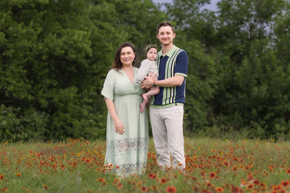 Two people stand together in a blooming red poppy field wearing light colored clothing on a summer day.