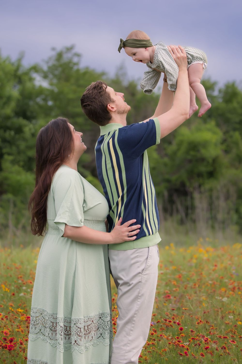A family shares a tender moment together in a wildflower field filled with vibrant red blooms on a sunny day.