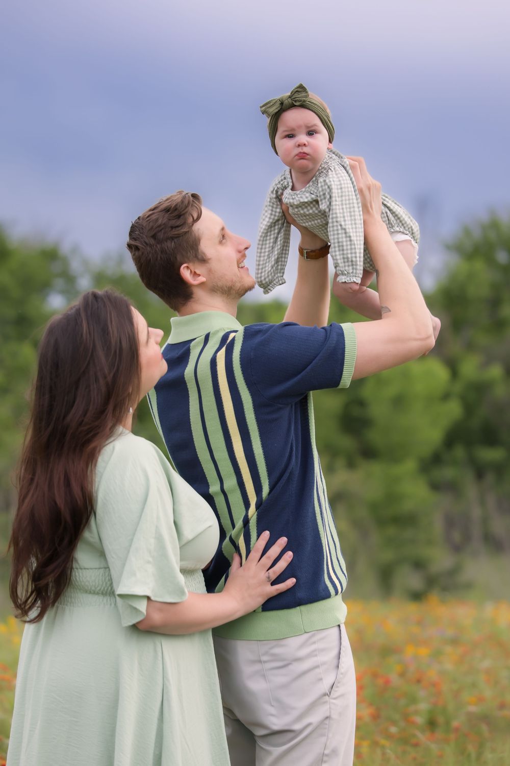 A joyful family moment captured outdoors in a meadow with orange wildflowers and green foliage.