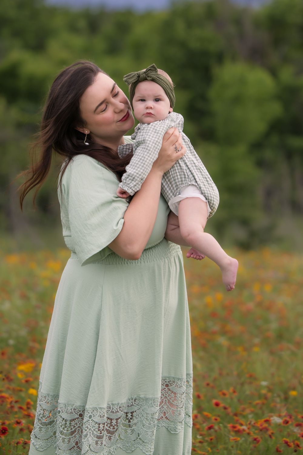 A tender moment captured in a wildflower field, wearing a sage green dress with lace details on a bright spring day.