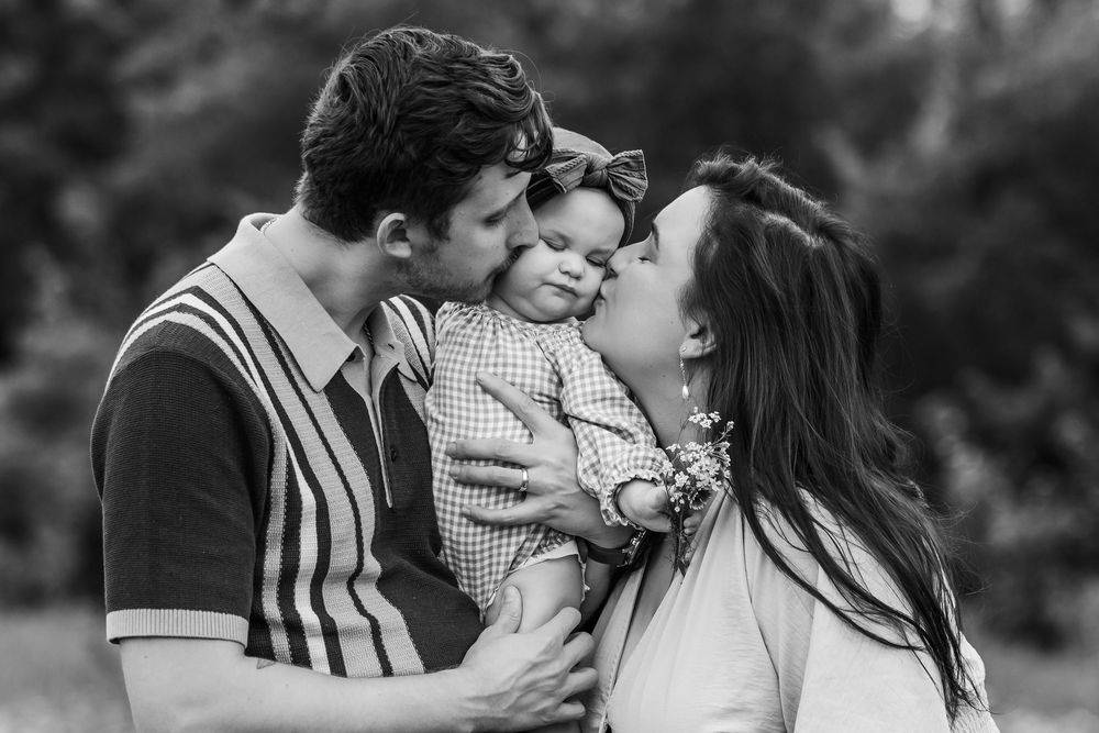 A tender black and white portrait showing parents sharing an affectionate moment with their young child.