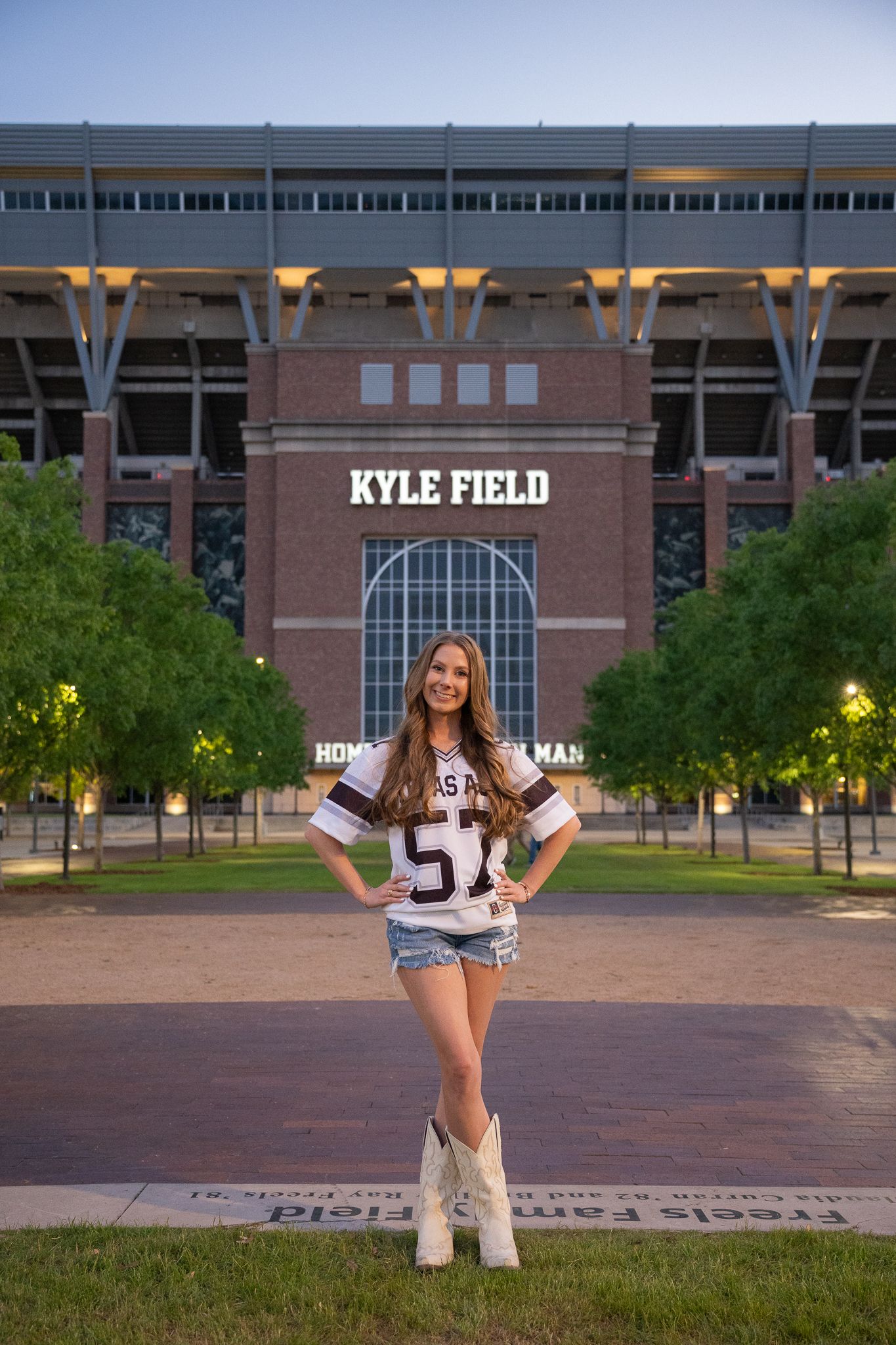 Student stands in front of Kyle Field stadium entrance at Texas A&M wearing a maroon jersey and white boots.