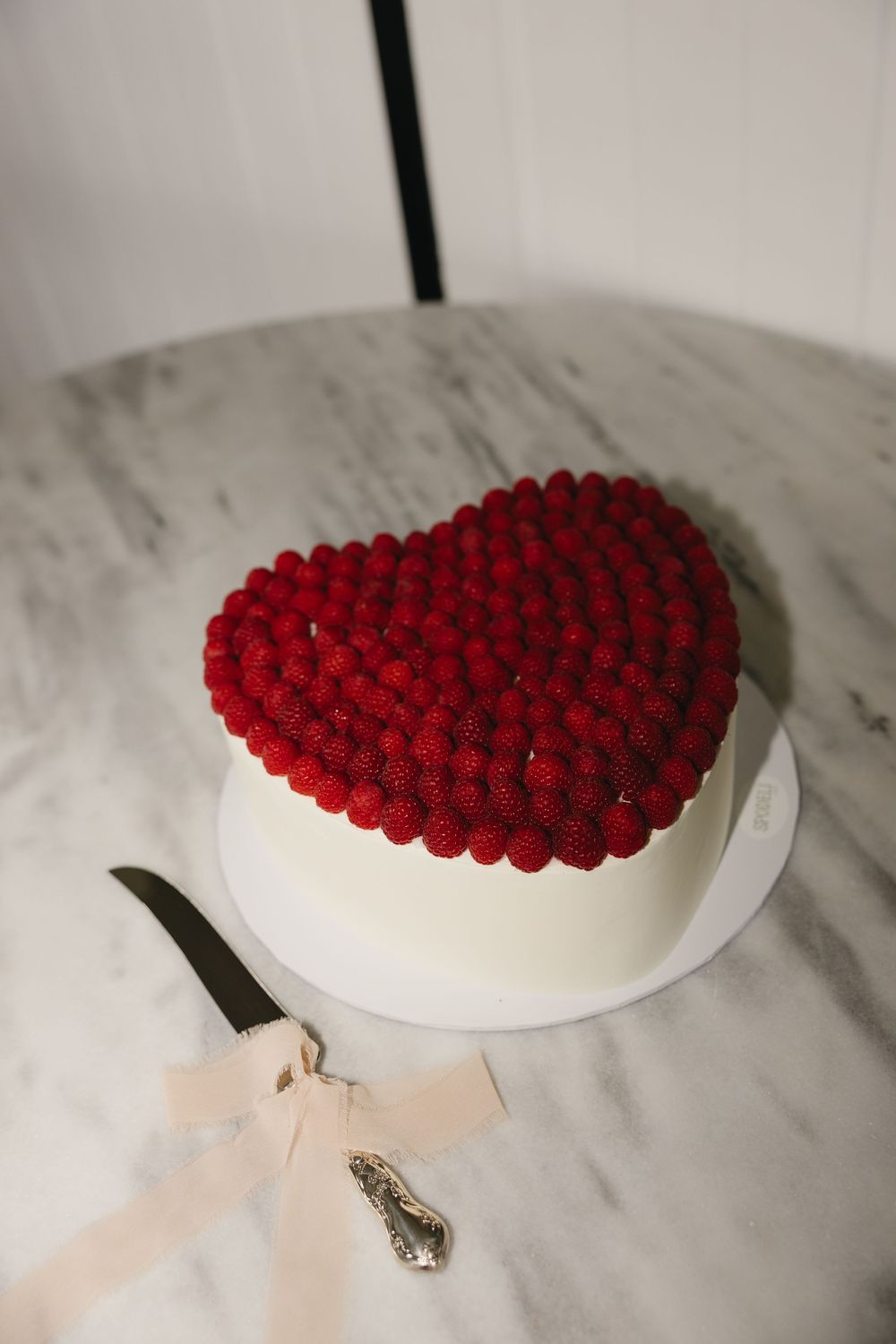 Red raspberries arranged in a heart shape on a white plate against marble background create an elegant dessert presentation.