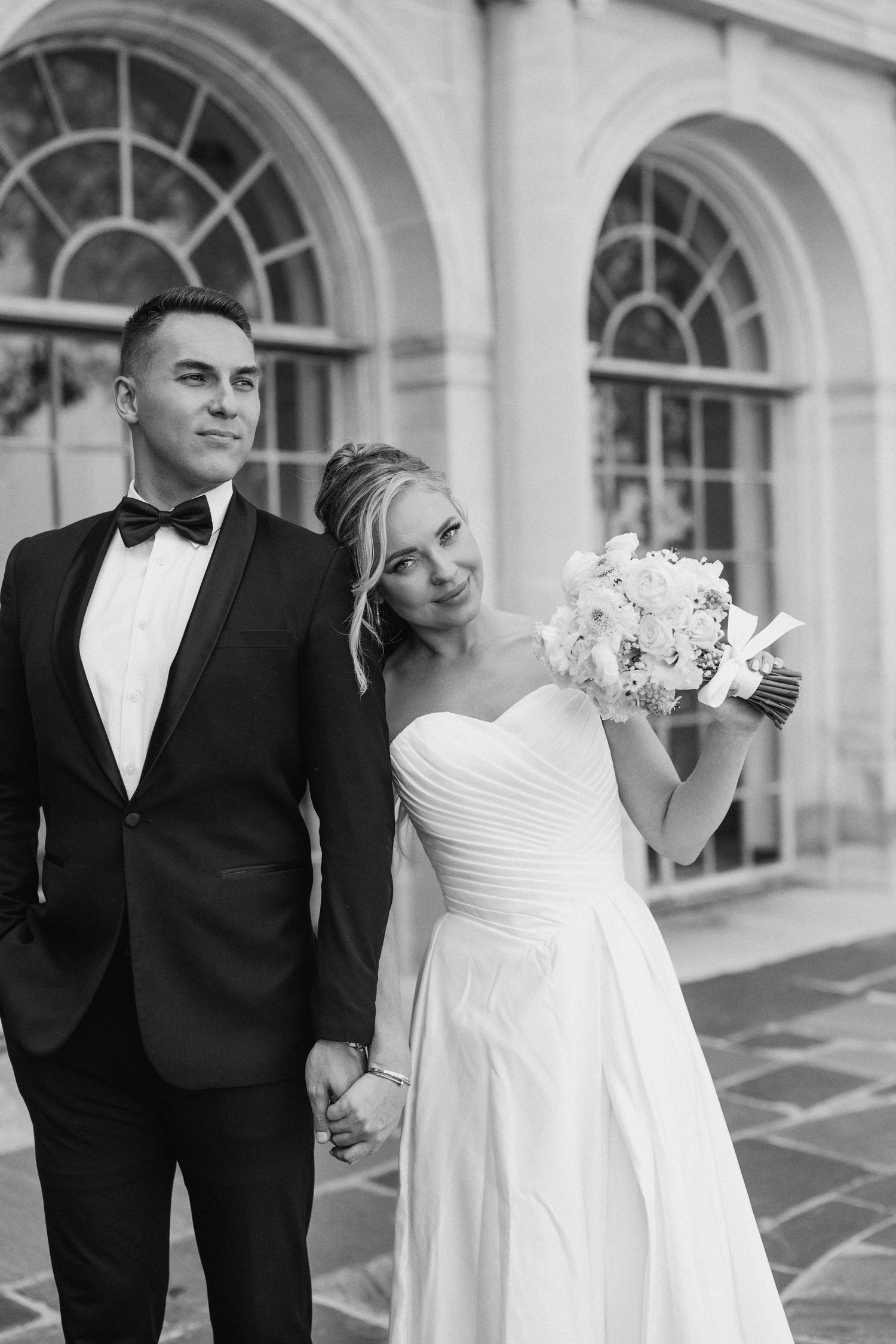 Black and white wedding portrait of a couple in formal attire posing together with the bride holding a bouquet.