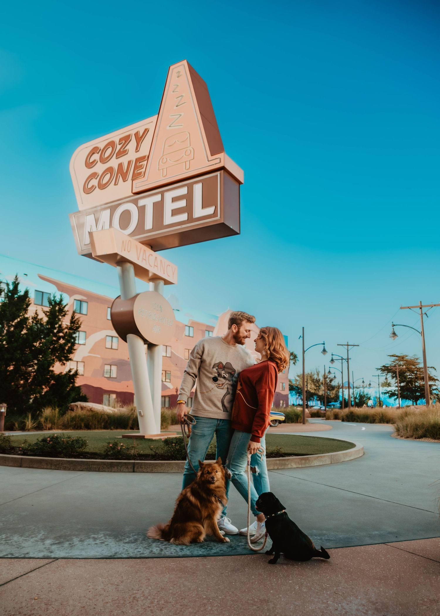 John & Emily anniversary photos at Disney's Art of Animation with Cozy Cone Motel in background & their dogs. Cred: LexTakePix