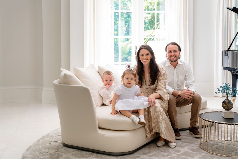 A family sits together on a modern cream-colored curved sofa in a bright, sunlit living room.