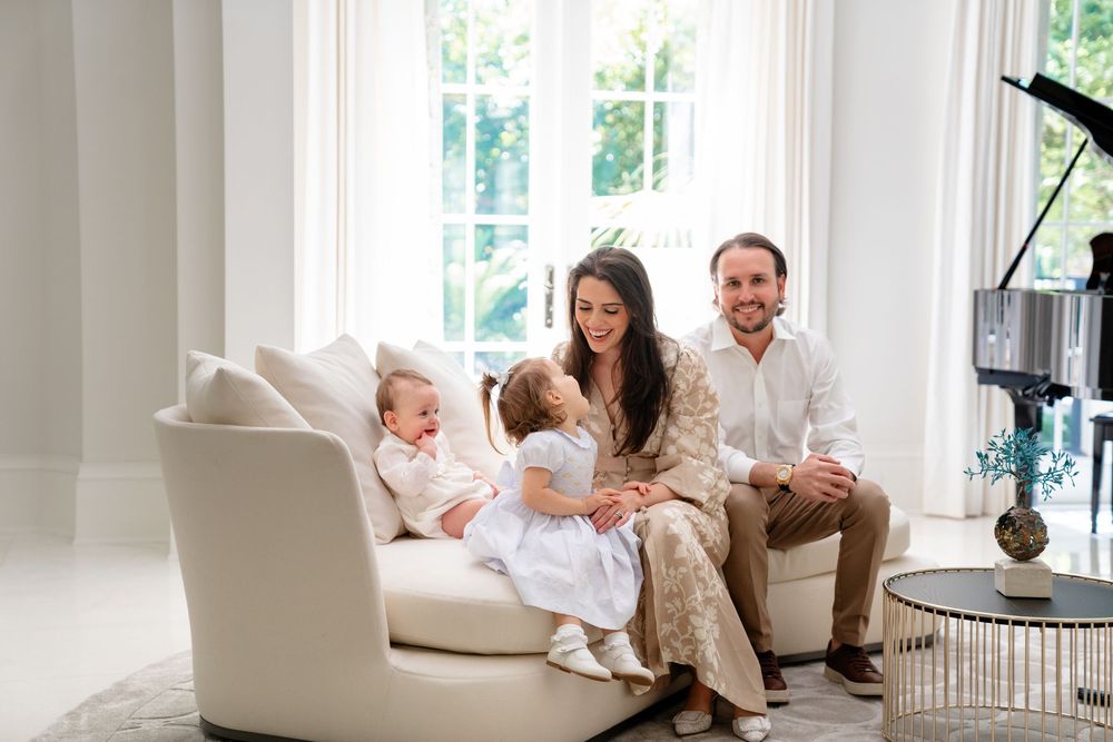 Family relaxes together on white sofa in bright sunlit living room during cozy lifestyle photoshoot.