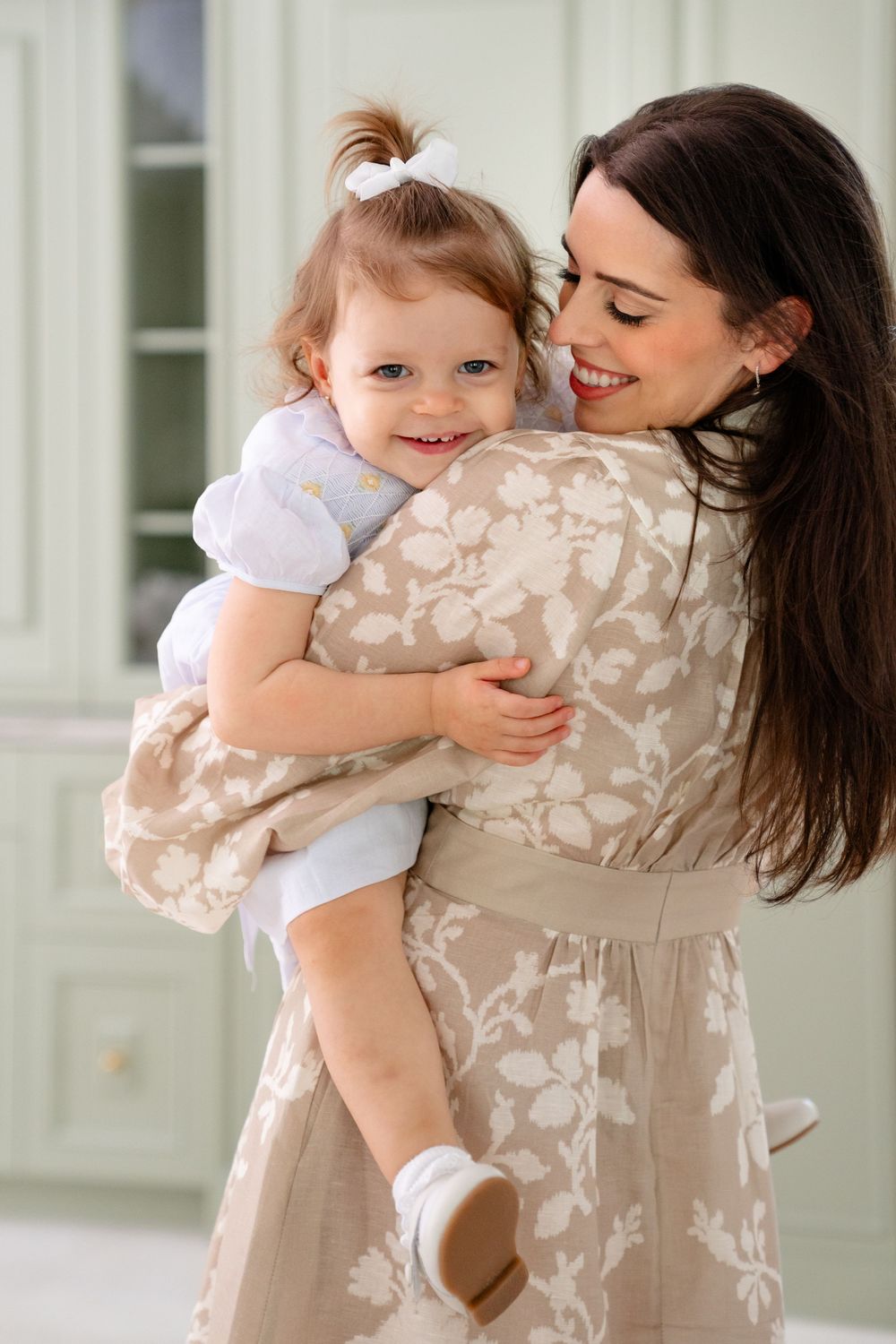 A tender moment between parent and child as they embrace and smile while wearing light beige and white clothing.