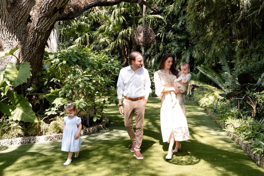 A family walks together on a lush green path surrounded by tropical plants and trees in a garden setting.