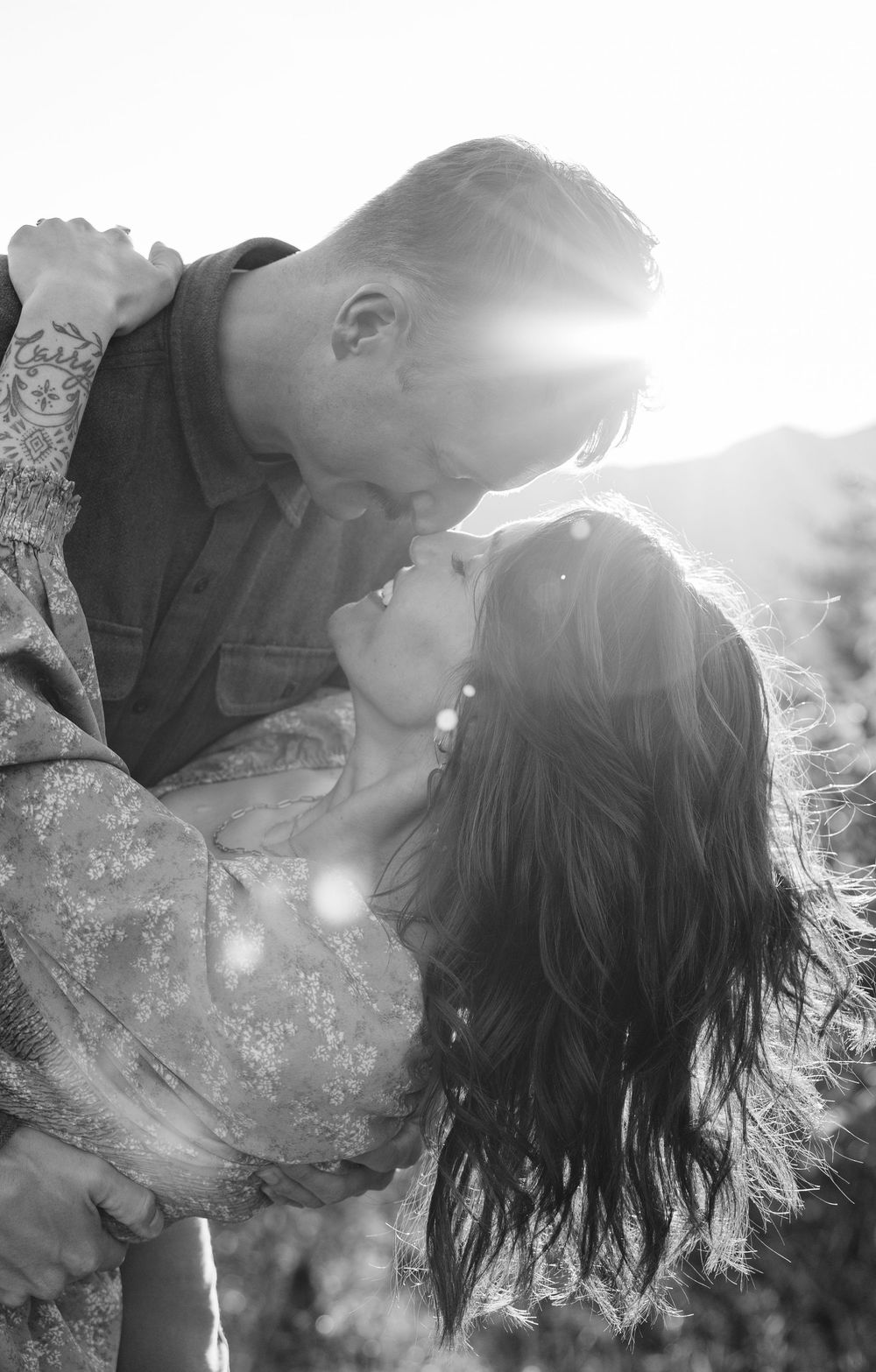 A romantic black and white photo of a couple in an intimate embrace with sunlight streaming behind them.