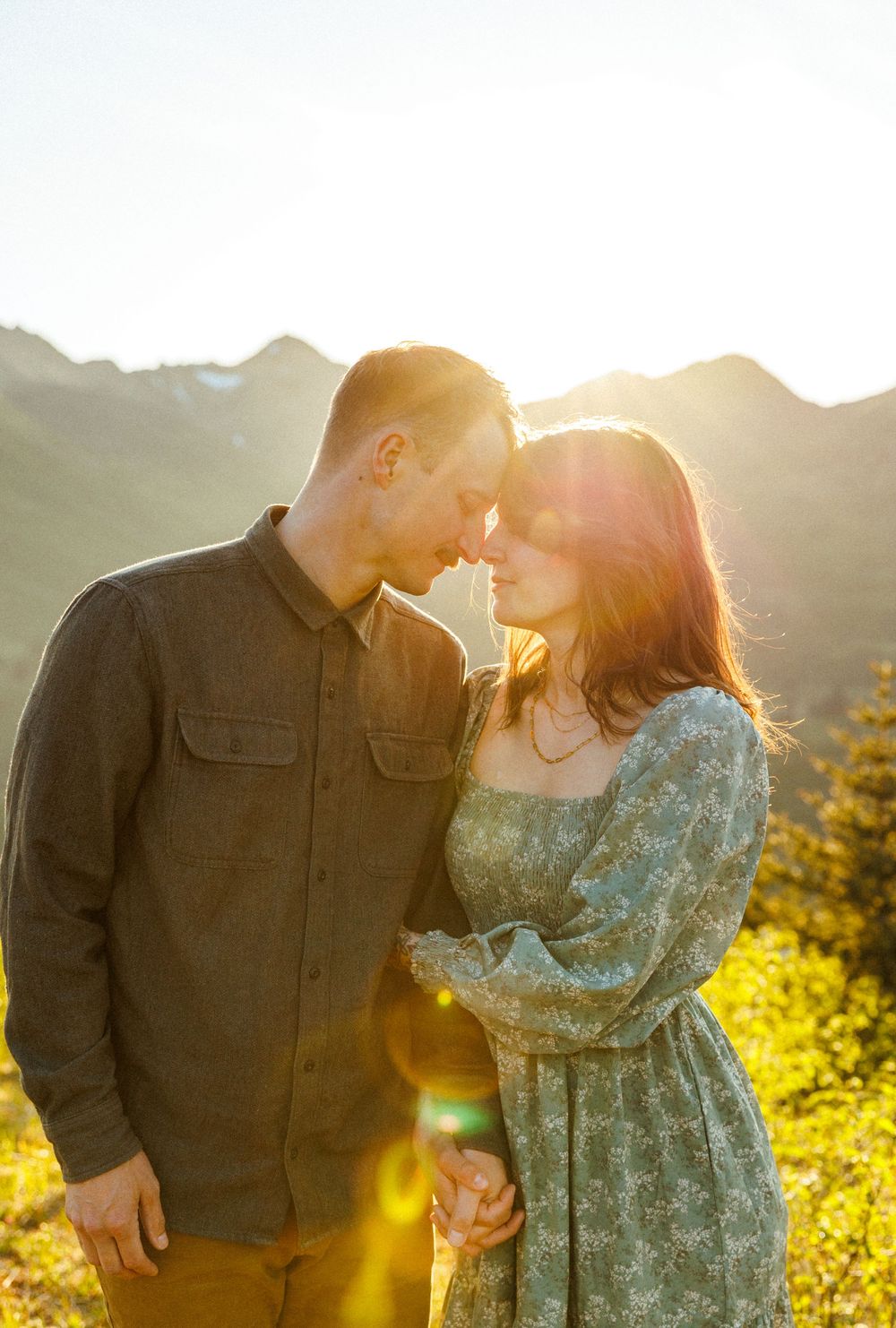 Intimate couple shares tender moments in golden sunlight with mountain views behind them.