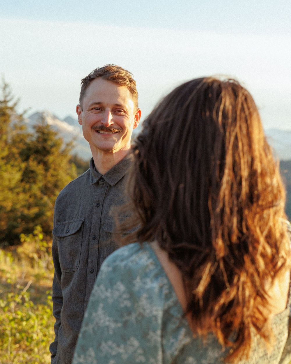 A romantic couple shares a joyful moment outdoors against a mountainous backdrop.