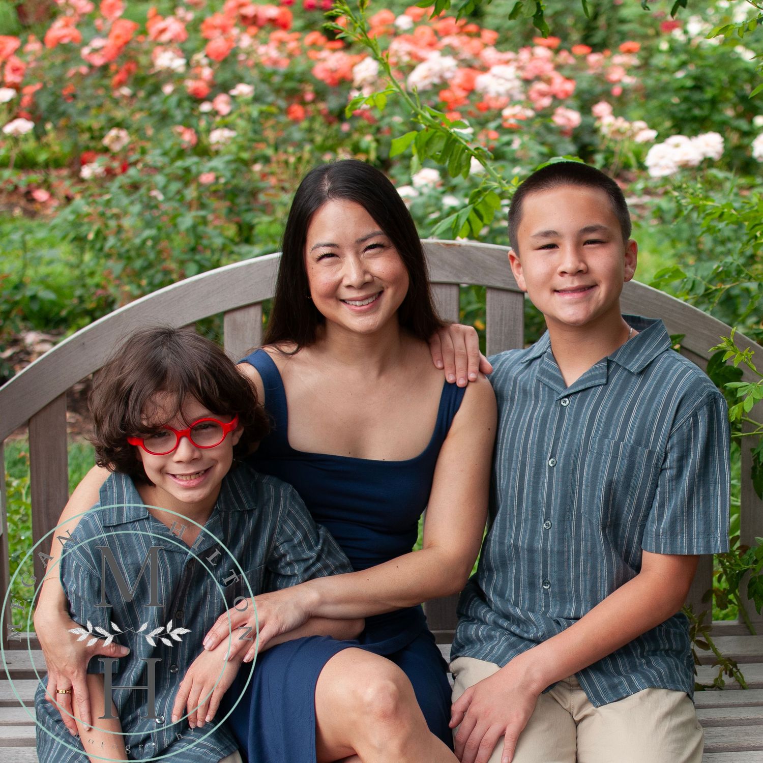 Family members enjoying time together on a wooden bench surrounded by blooming flowers in an outdoor garden setting.