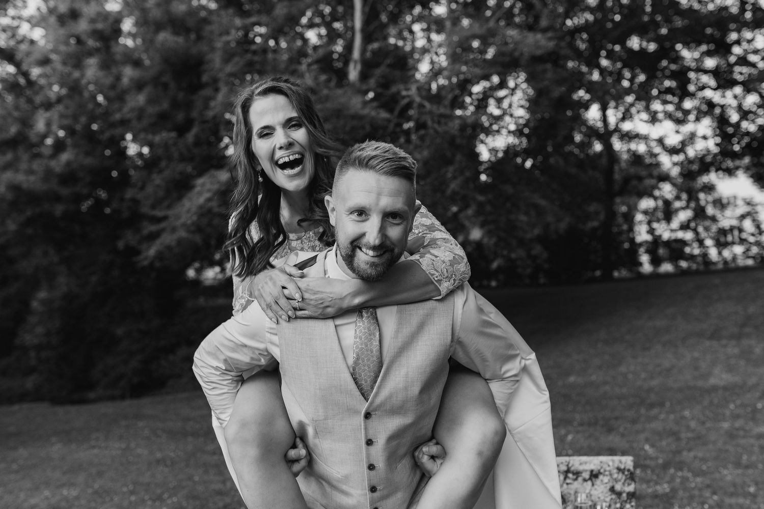 A joyful black and white photo of a piggyback moment outdoors in a park setting.