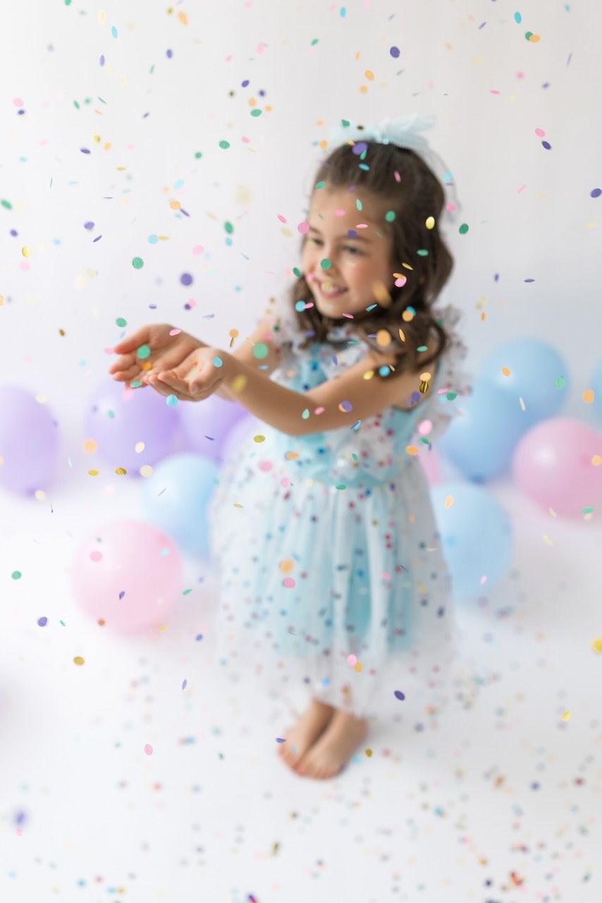 Studio portrait of girl blowing confetti from her hands in a magical birthday moment.